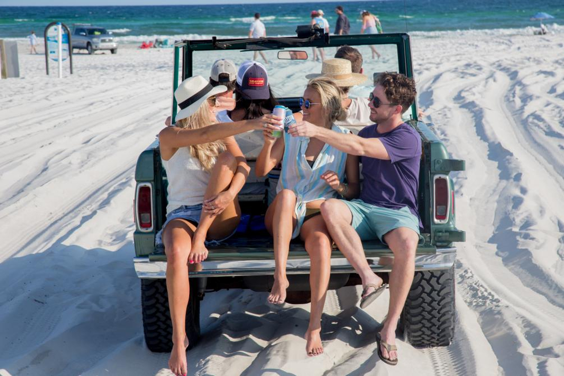 Friends enjoying beer on back of car at beach